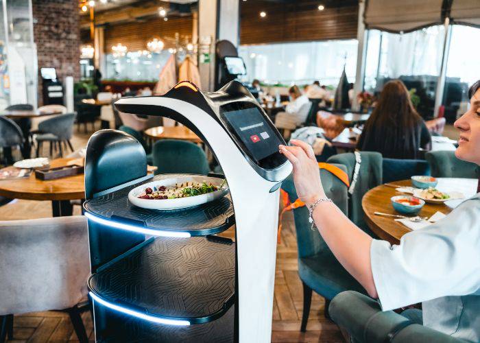 A cat-shaped robot waiter at a family restaurant in Japan. A guest is tapping buttons on the screen.